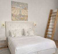 Bright bedroom with a bed, painting on the wall, nightstand, and wood-patterned floor.