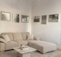 Living room in a 3-room apartment with a beige sofa, table, paintings, and a floor with a wooden decor.