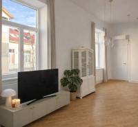 Living room in a 3-room apartment with wood-patterned flooring, a television, and large windows.