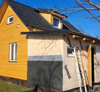 A cottage in Kráľovce Krnišov with wooden cladding and an unfinished extension against the backdrop of a blue sky.