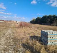 Plots - housing in Nové Zámky, gravel road, greenery, blue sky, and building materials.