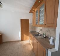 A kitchen in a 3-room apartment with wooden cabinets and white appliances on tiles.