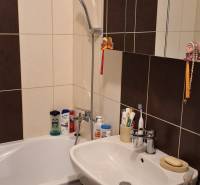 A bathroom with a shower, sink, and cabinet in a 4-room apartment, predominantly dark tiles.