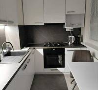 A kitchen with white cabinets and a table in a two-room apartment with a wood-patterned floor.