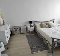 A bedroom in a two-room apartment with light furniture and a wooden decor floor.