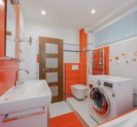 Orange-white bathroom in a 2-room apartment with a washing machine and a sink.
