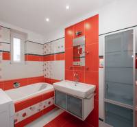A bathroom in a 2-room apartment with orange and white tiles and a bathtub.