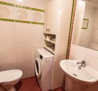 Bathroom in a 2-room apartment with a washing machine, sink, and toilet, tiled with white tiles.