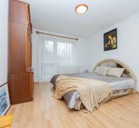 A bright bedroom in a family house with a wood-patterned floor and a large bed.