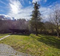 The garden of a family house in Tŕstie with a lawn, trees, and a paved walkway.