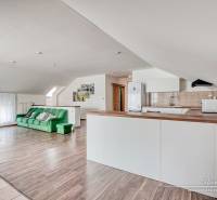 Living room with kitchen, green sofa, white furniture, wooden decor flooring.