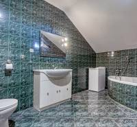 A bathroom in a family house with a bathtub, green tiles, and white furniture.