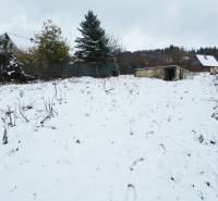 Snow-covered recreational plots in Považská Bystrica with a view of the forest and house.