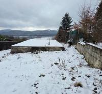 Snow-covered recreational plots in Považská Bystrica with a view of the mountains and planted trees.