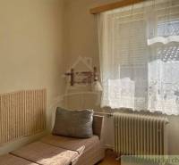 A simple room in a family house with a lounger and decorative curtains on the window.