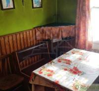 A room in a family house with wooden paneling, a floral tablecloth, and curtains.