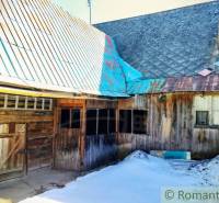 A wooden family house in Osturňa with a metal roof and remnants of snow in the yard.
