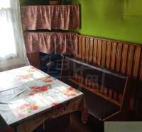 Dining area in a family house with wooden paneling, curtains, and a floral tablecloth.