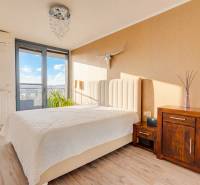 A bedroom in a 3-room apartment with a bed, dresser, decorations, and a wooden-patterned floor.