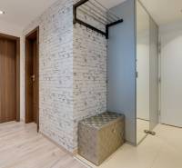 A hallway with a wood-patterned floor, white wall, and glossy bench in a three-room apartment.