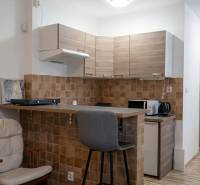 A kitchenette in a studio apartment with a wooden decor floor, light cabinets, equipped with a bar stool.