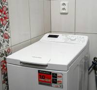 A washing machine in a studio apartment, floral patterned tiles, and a white socket on the tiles.