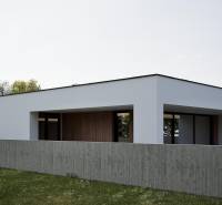 A family house in Nesvady with a white facade and wooden accents behind a concrete fence.
