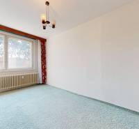 A room in a 2-room apartment with a window, radiator, and curtains with a floral pattern.