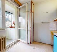 A kitchen with white cabinets, light, and a view of the balcony in a 2-room apartment.