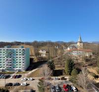 A view of Banská Bystrica from Kalinčiakova Street, next to a 2-room apartment, with a church and an apartment building.