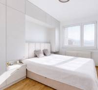 A bedroom in a 3-room apartment with a wood-patterned floor, white furniture, and a large window.