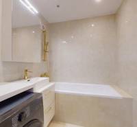 A bathroom in a 3-room apartment with a bathtub, golden faucets, and a washing machine.