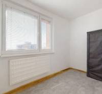 A room in a 3-room apartment with a radiator and a wardrobe, with a light wall and carpeted floor.