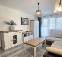 A living room in a two-room apartment with a wood-patterned floor, a sofa, and white furniture.