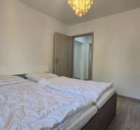 Bedroom in a 2-room apartment with a double bed, light-colored wall, and floor with wood decor.