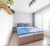 Bright bedroom with a double bed, blue curtains, and a wooden-patterned floor.