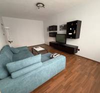 Living room with a TV, blue sofa, and wood-patterned flooring in a 3-room apartment.