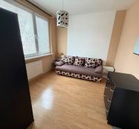 A room with a sofa, a dresser, and a wooden-patterned floor in a three-room apartment.