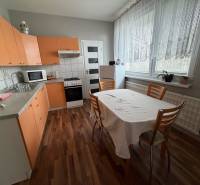 A kitchen with orange cabinets, a dining table, and a wood-patterned floor in a three-room apartment.