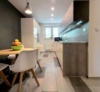 A kitchen in a 2-room apartment with a dining table, tiles, and lights above the countertop.