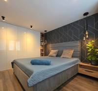 Bedroom in a 2-room apartment with an upholstered bed, patterned wall, and floor with wood decor.