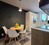 A kitchen in a 2-room apartment with white furniture and a dining table with fruit.