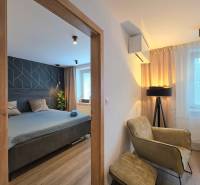 A two-room apartment with a wooden decor floor includes a bedroom, an armchair, and a lamp.