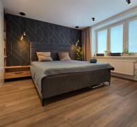 A bedroom with a dark accent wall, a large bed, and a wood-patterned floor.