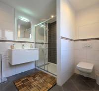 A bathroom with a wooden decor floor, a shower corner, and a wall-mounted toilet in a 2-room apartment.