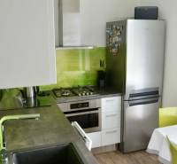 A kitchen in a 2-room apartment with a stainless steel appliance, green tiles, and a wooden decor floor.