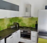 A kitchen with white cabinets and green tiles, a gas stove, and a refrigerator in a 2-room apartment.