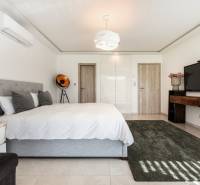 A bedroom in a family house with a white bed and a large TV on the wall.