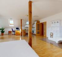 Attic interior of a family house with a tiled stove, a work corner, and a floor with a wooden decor.