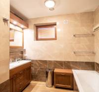 A bathroom in a family house with a bathtub, sink, shower corner, and a floor with a wooden decor.